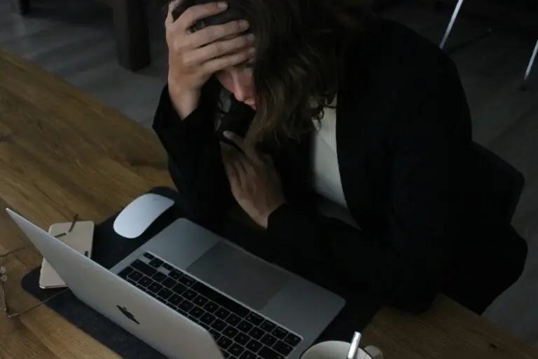 Gestresste Frau mit einer Hand am Kopf vor dem Laptop
